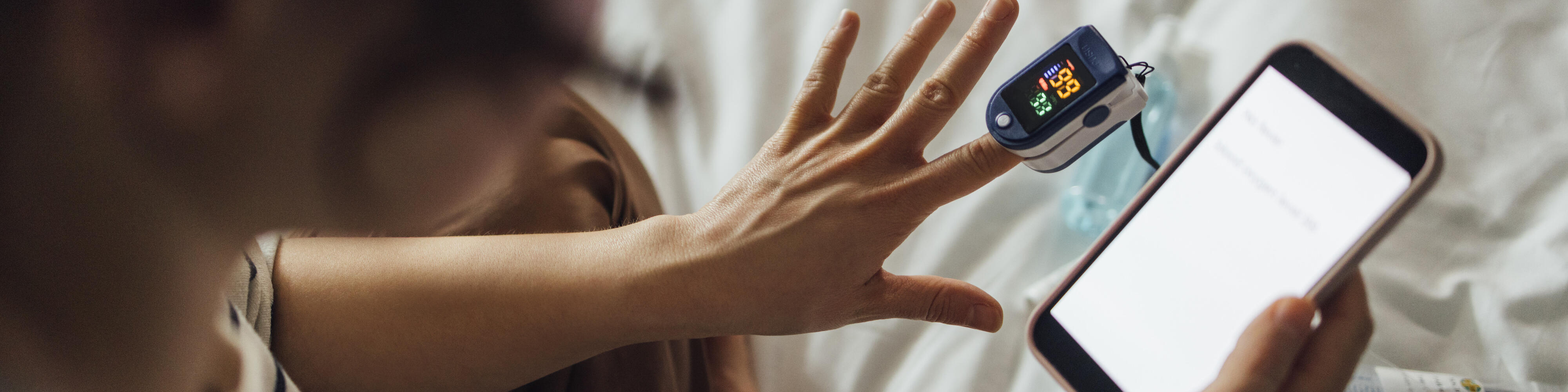 Eine von oben aufgenommene Aufnahme einer nicht erkennbaren Frau, die den Sauerstoffsättigungsgrad ihres Blutes misst.