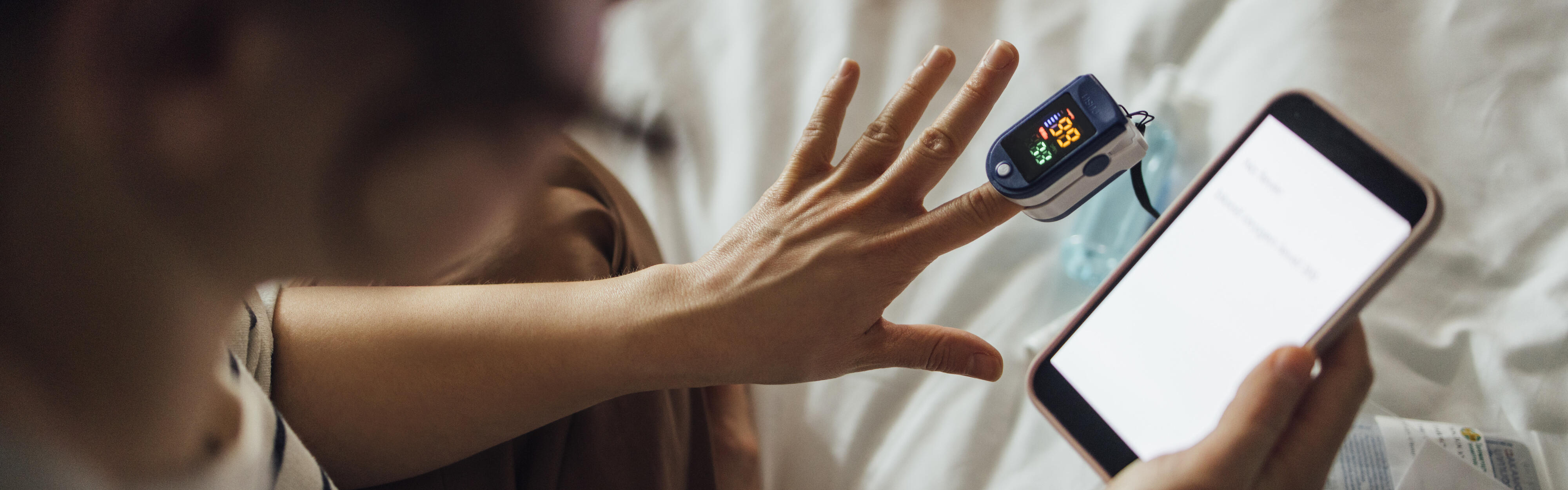 Eine von oben aufgenommene Aufnahme einer nicht erkennbaren Frau, die den Sauerstoffsättigungsgrad ihres Blutes misst.
